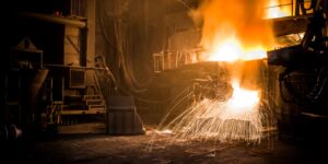 Steelmaking furnace area with molten metal and sparks inside an industrial plant.