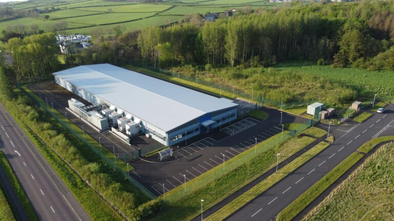 Aerial view of a long single-storey technical building with a row of generators along one side and electrical kiosks near the entrance