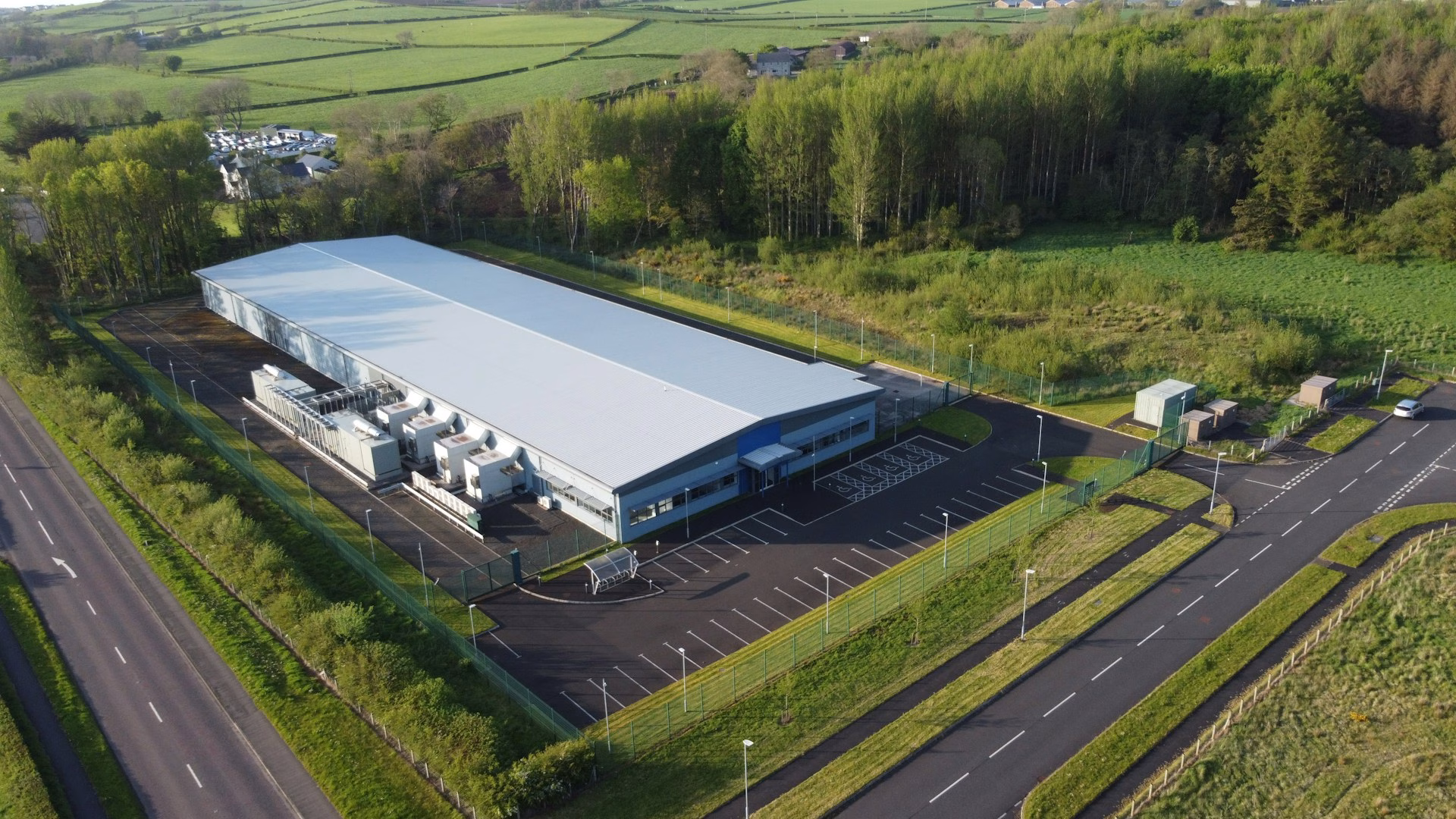 Aerial view of a long single-storey technical building with a row of generators along one side and electrical kiosks near the entrance