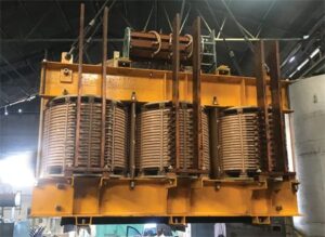 Three exposed transformer windings and support structure inside an industrial workshop.