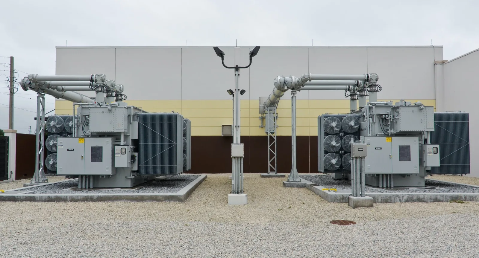 Two oil-filled power transformers with cooling fans side by side in a utility substation